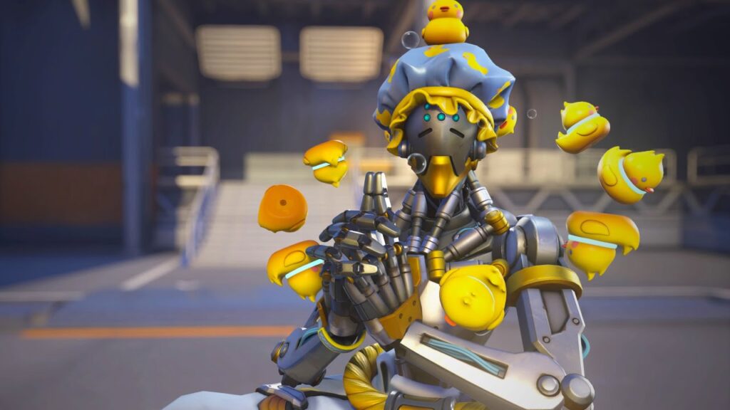 Zenyatta in his Bathmaster skin from Overwatch 2, wearing a blue shower cap with yellow duck patterns and surrounded by floating rubber ducky orbs, striking a meditative pose in an industrial setting.